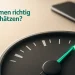 Nahaufnahme eines analogen Tankanzeigers, dessen Nadel knapp vor der Reserve leuchtet, im Hintergrund ein unscharfes Smartphone.