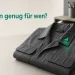 Gefaltete Arbeitsjacke auf grauem Tisch mit einem leuchtend grünen Anstecker als einzigem Farbakzent, symbolisiert den passenden Einstiegstarif.